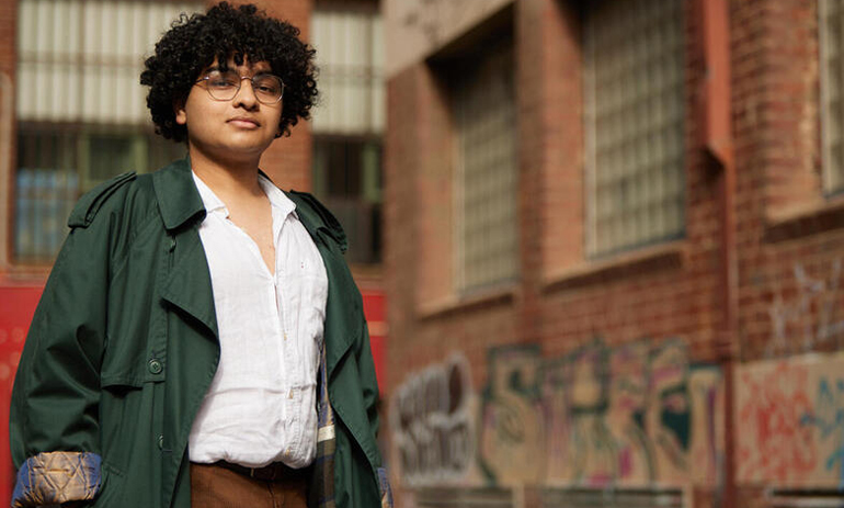 A young man stands in front of a brown brick building