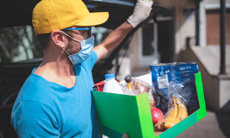 Man wearing facemask carrying a box of groceries